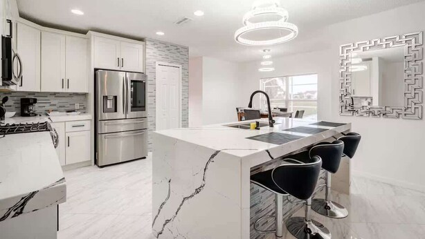 Une cuisine moderne avec des meubles blancs, un îlot central, des appareils en acier inoxydable et un miroir décoratif.