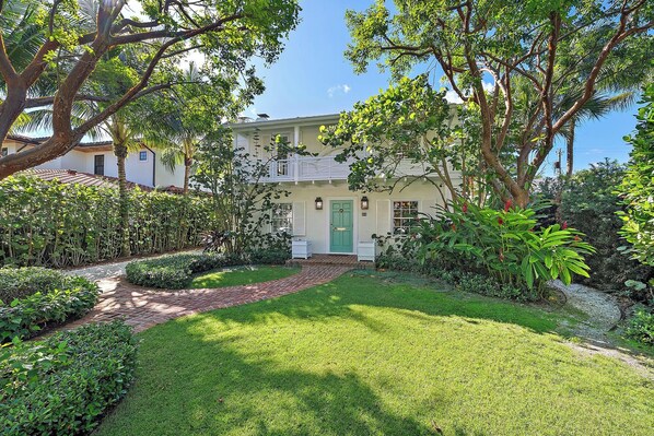 A two-story house with a green door, surrounded by lush greenery and a well-maintained lawn.