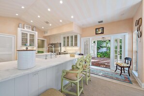 A modern kitchen with white cabinetry, a central island, and a dining area with green chairs.