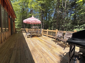 Une terrasse en bois avec une table et des chaises, un barbecue et un parasol rose.