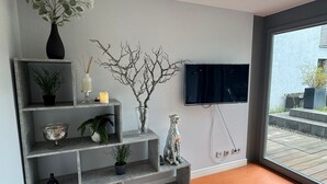 Un saló modern amb un moble d'estanteries gris, un televisor penjat a la paret i una finestra gran.