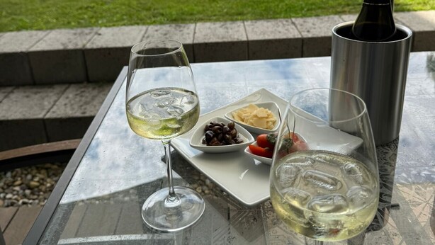 Una taula de vidre amb dues copes de vi, una ampolla i un plat d'olives i formatge.