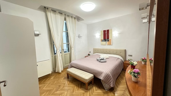 A bedroom with a bed, bench, bedside table, and a potted plant.