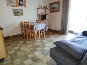 A room with a checkered floor, a dining table with chairs, a television on a wooden shelf, a radiator, and a bed with pillows. - Studio with parking for 2-3 people in Briançon center 700 m from cable car (Briançon)