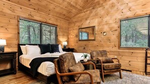 Un dormitorio con paneles de madera, una cama, dos sillones, una mesita de noche, un espejo y un ventanal con persianas.