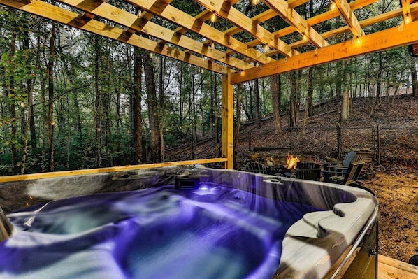 A hot tub in a wooden gazebo surrounded by a forest.