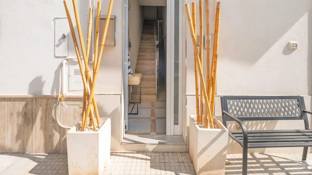 A building entrance with a staircase, two planters with bamboo sticks, a bench, and a door with a sign. - Casa Marelì Eleganza e Vista Mozzafiato a Porto Cesareo (Porto Cesareo)