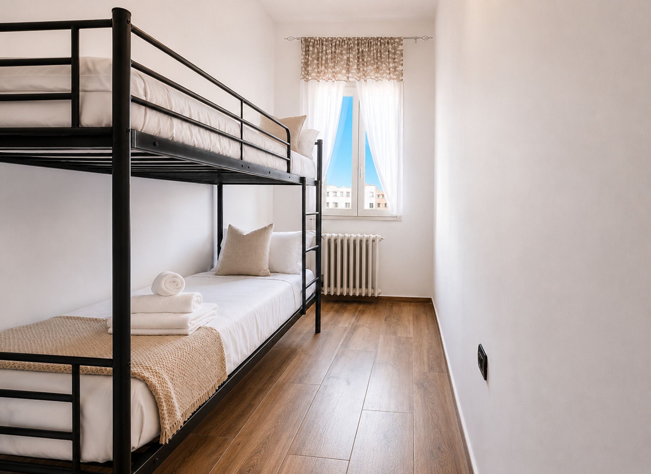 A bunk bed room with a radiator, a window with a view, and wooden flooring.