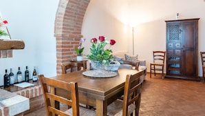 A dining area with a wooden table, chairs, a vase of flowers, and a brick wall. - Apartment 'Villa Tiberini 2' with Garden View, Shared Pool and Wi-Fi (Torrita di Siena)