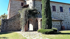 A stone building with a chimney, arched entrance, and a tall cypress tree in front. - Apartment 'Villa Tiberini 2' with Garden View, Shared Pool and Wi-Fi (Torrita di Siena)