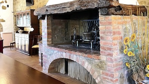 A rustic stone fireplace with a brick arch, a wooden table, and a vase with sunflowers. - Apartment 'Villa Tiberini 2' with Garden View, Shared Pool and Wi-Fi (Torrita di Siena)