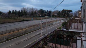 A street view with a road, a fence, and a building with a balcony.