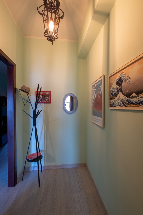 A hallway with a wooden floor, a black coat stand, a framed picture of a wave, and a round mirror on the wall.