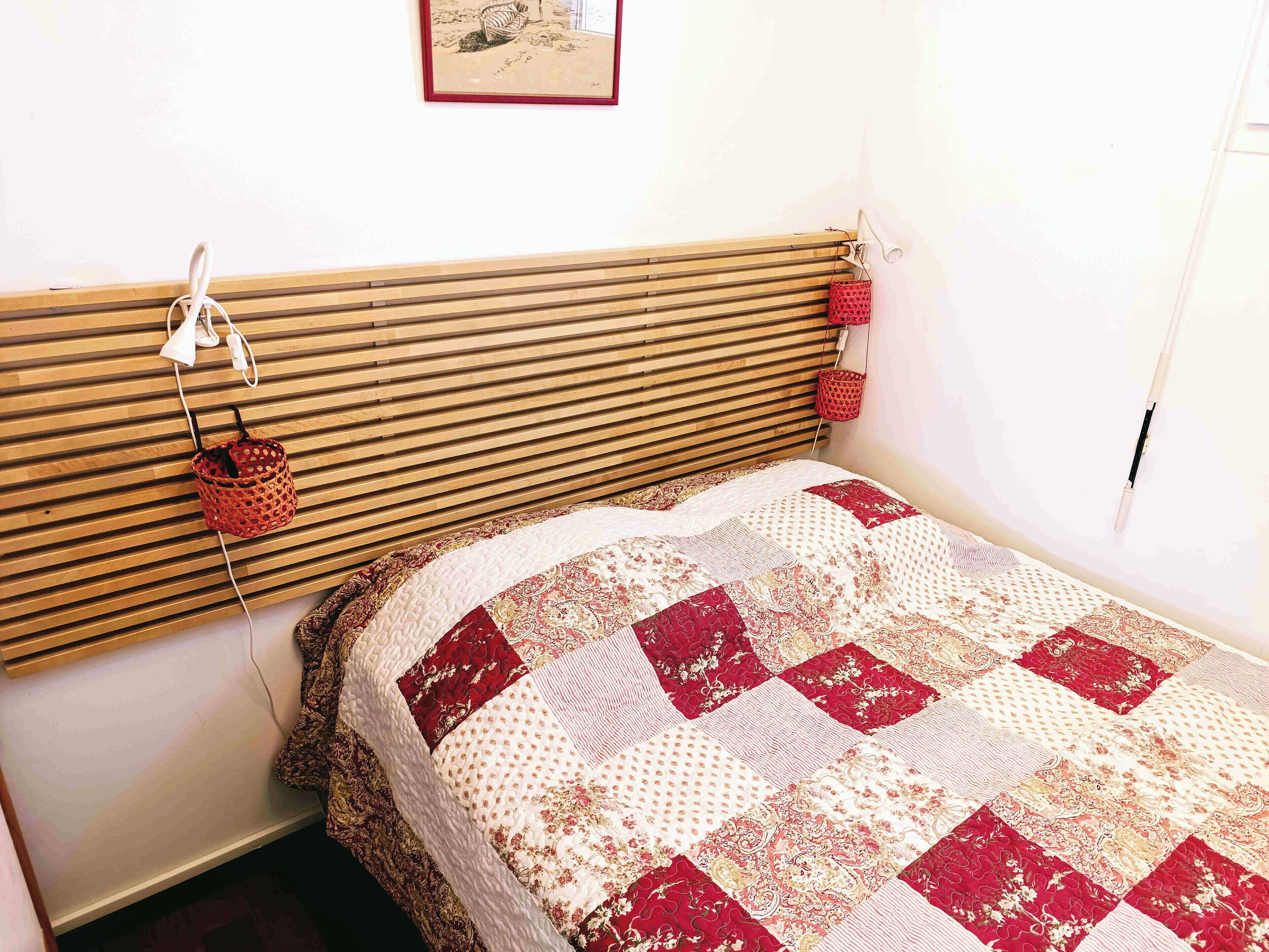 Un dormitorio con cabecera de madera con listones, colcha acolchada y una cesta roja colgada en la pared.