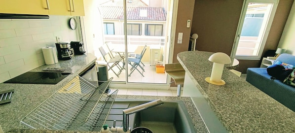 A kitchen with a sink, countertop, and chairs. There is a window with a view of buildings outside.