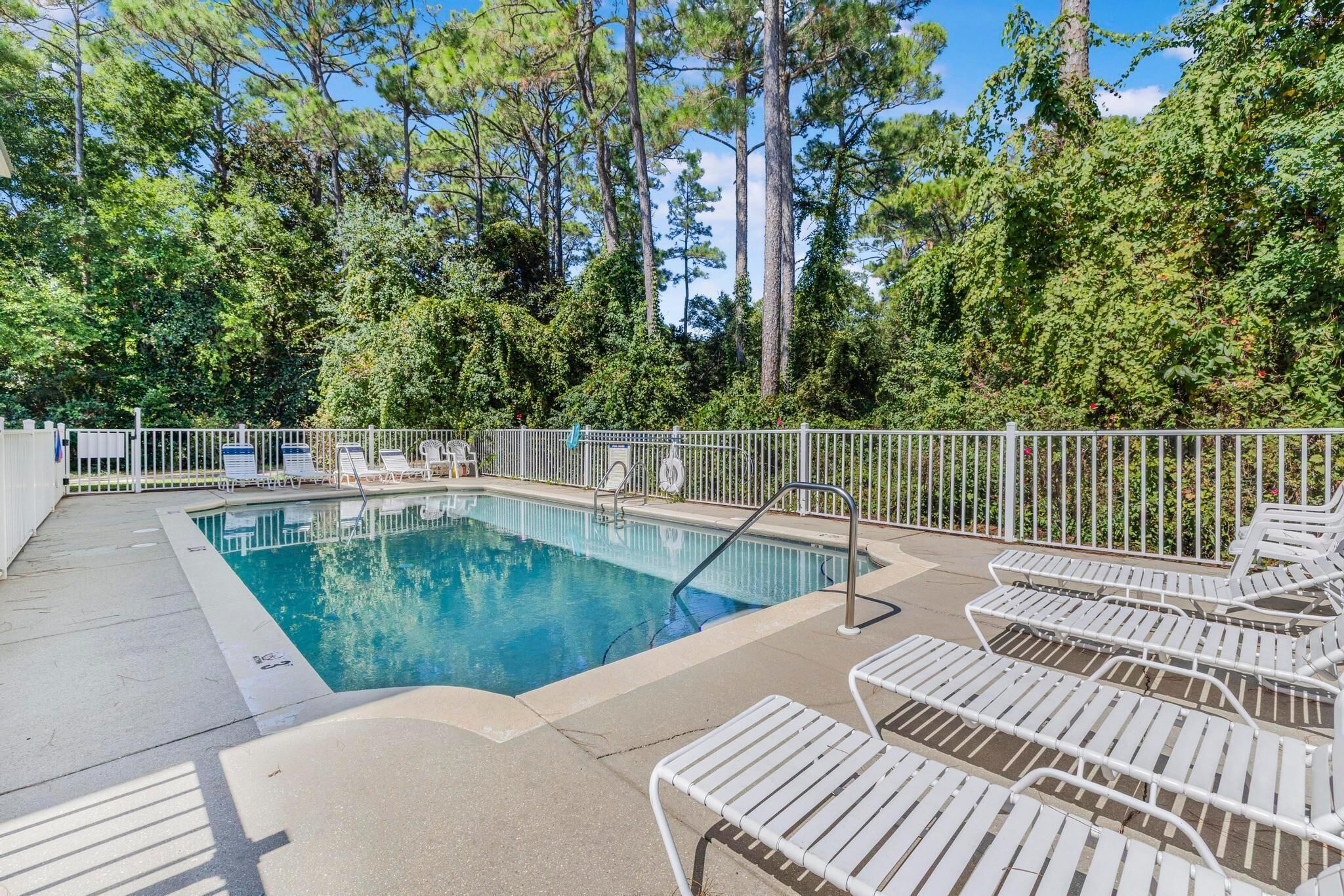 Une piscine dotée de chaises longues et d’un espace délimité par une clôture, le tout entouré d’arbres.