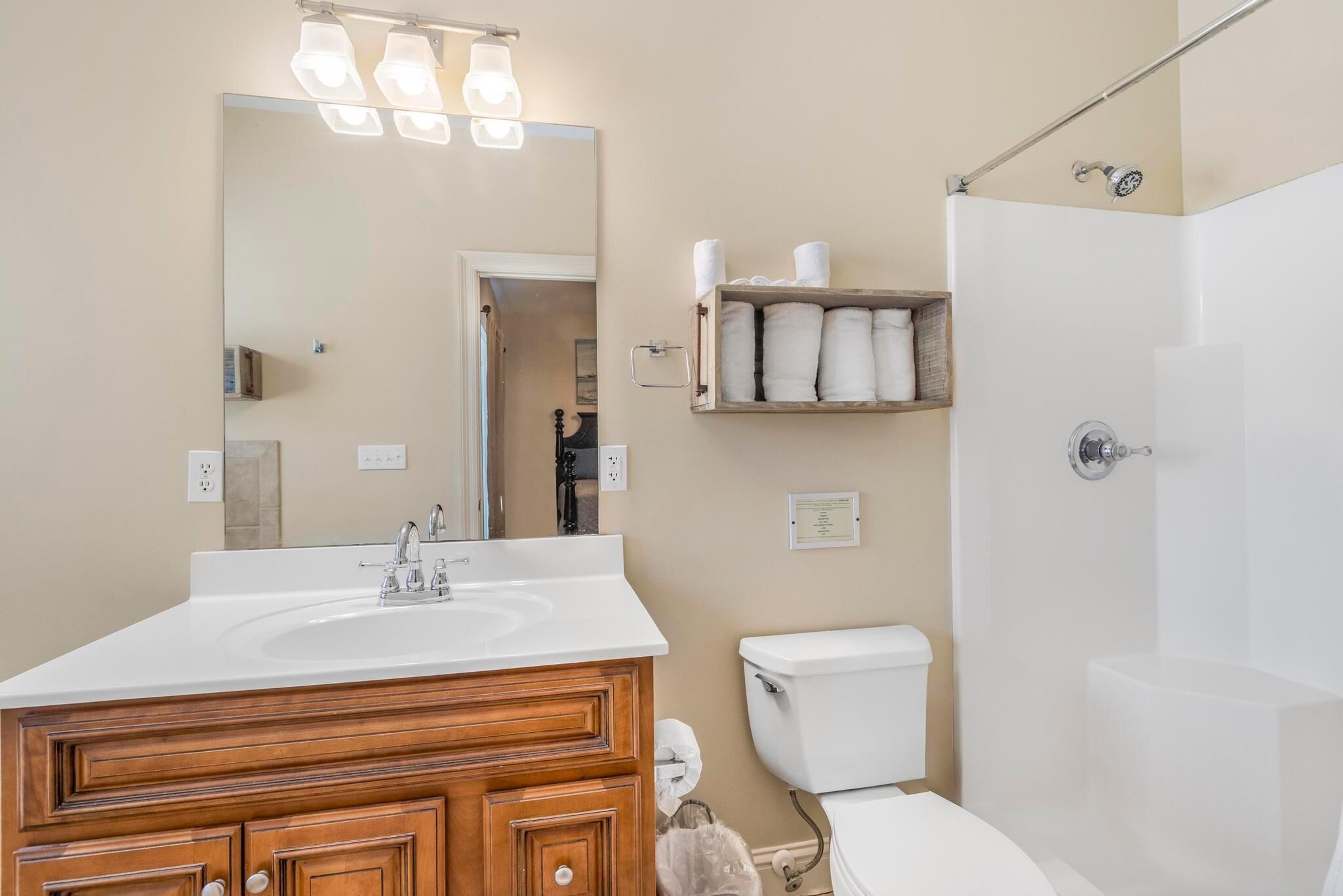 Une salle de bain avec un lavabo blanc, un meuble-lavabo en bois, des toilettes, une douche et un miroir avec éclairage.