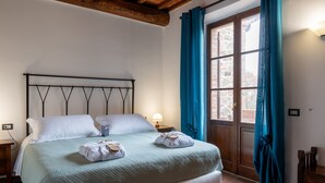 Een net opgemaakt bed met een hoofdbord, een bedlampje en een raam met gordijnen.