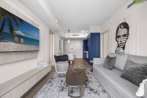 A modern living room with a sofa, coffee table, and a painting of a beach scene. - The Avenue Luxury Residences Coral Gables (Coral Gables)