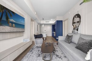 Una sala de estar moderna con un mural de playa, un sofá gris, una mesa de centro y un comedor con una mesa y sillas blancas.