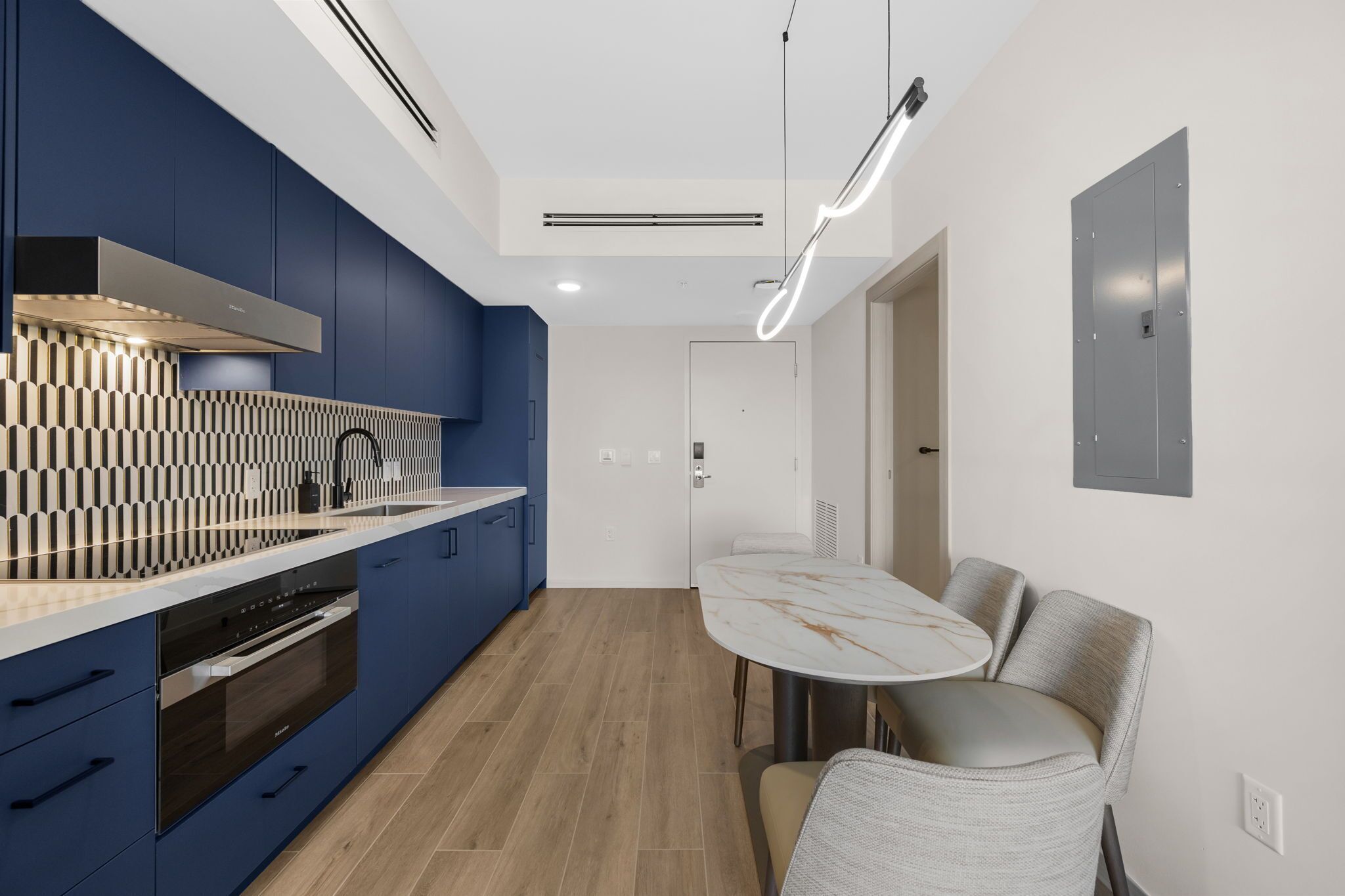 A modern kitchen with blue cabinets, a marble countertop, and a dining area with a round table and chairs.