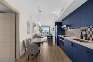 Una cocina moderna con gabinetes azules, una encimera blanca y un grifo negro. Hay una zona de comedor con una mesa y sillas.