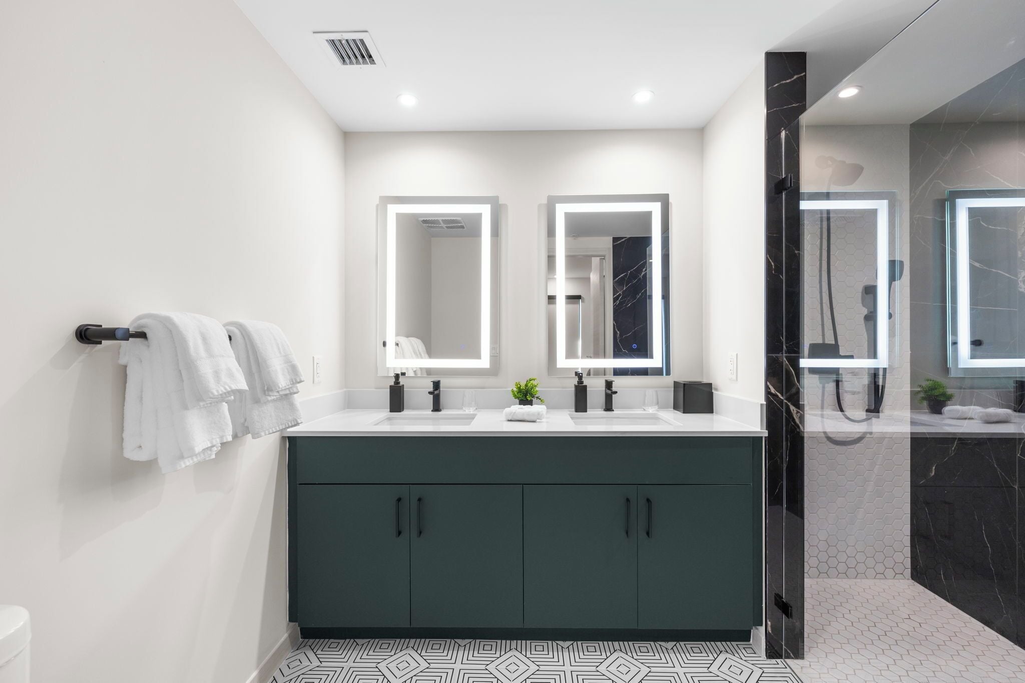 A modern bathroom with a dark green vanity, two mirrors, a white sink, and a glass-enclosed shower.