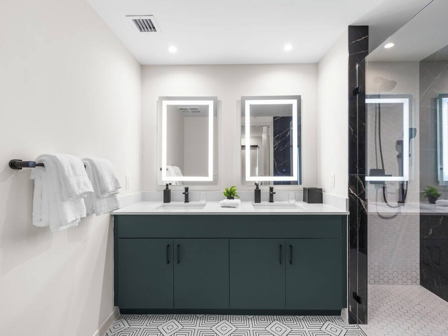 A modern bathroom with a dark green vanity, two mirrors, a white sink, and a glass-enclosed shower.