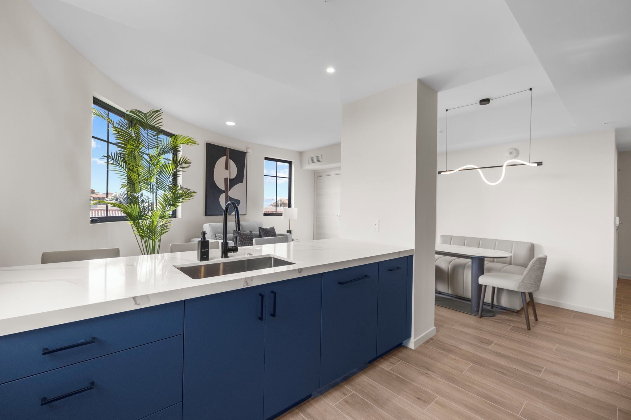 A modern kitchen with a white countertop, blue cabinets, and a dining area with a table and chairs.