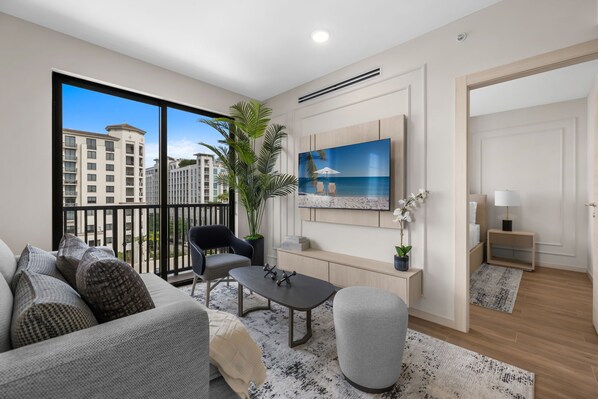A modern living room with a large window, a flat-screen TV, a dining table, and a sofa. - The Avenue Coral Gables (Coral Gables)
