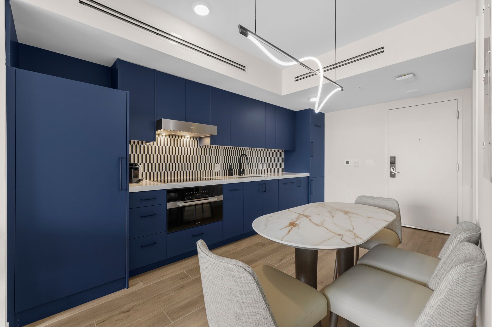 Une cuisine moderne avec des meubles bleus, un plan de travail en marbre et une table de salle à manger ronde, accompagnée de chaises.