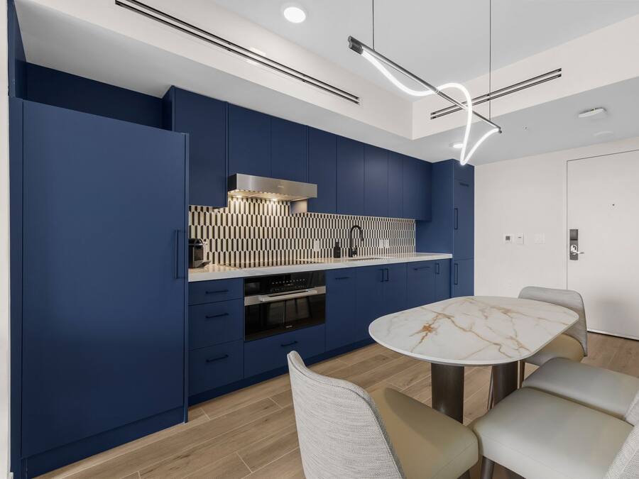 Une cuisine moderne avec des meubles bleus, un plan de travail en marbre et une table de salle à manger ronde, accompagnée de chaises.