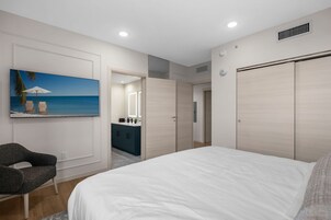 Un dormitorio con una cama grande, una silla, un cuadro de una playa, un tocador con espejo y un armario.