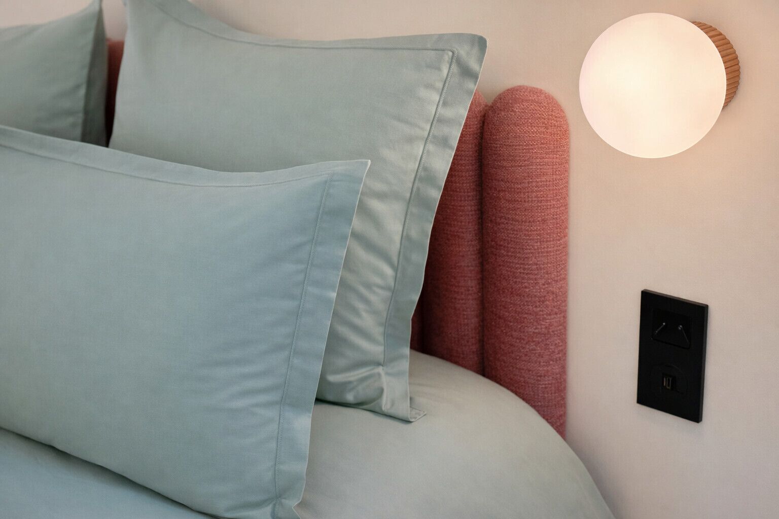 Un lit avec des oreillers, une lampe fixée au mur et une prise de courant.