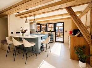 A modern kitchen with a central island, bar stools, pendant lighting, and a view to an outdoor deck.