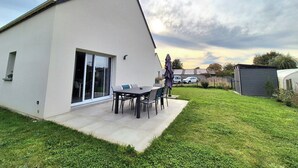 Une maison moderne dotée d’un patio, d’un espace extérieur aménagé et couvert, et d’une pelouse bien entretenue.