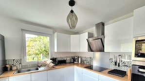 Une cuisine moderne avec des meubles blancs, un plan de travail noir et une fenêtre donnant sur la verdure à l’extérieur.