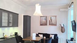 A modern kitchen with grey cabinets, a dining area with a wooden table and black chairs, and a living area with a black sofa and two framed pictures on the wall. - Studio in the heart of Nice, close to amenities (Nice)