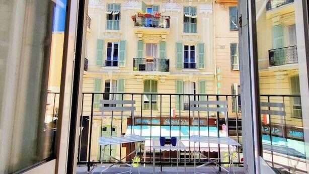 A balcony with a metal table and chairs, overlooking a building with multiple windows and balconies. - Studio in the heart of Nice, close to amenities (Nice)