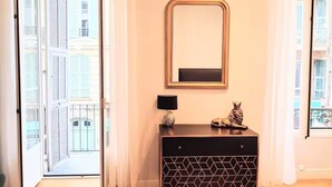 A room with a large window, a black cabinet with geometric patterns, a gold-framed mirror, and a small decorative lion statue. - Studio in the heart of Nice, close to amenities (Nice)