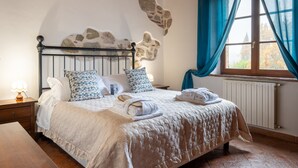 A bed with a headboard, pillows, a bedside table with a lamp, and a window with curtains. - Apartment 'Villa Tiberini 4' with Panoramic View, Shared Pool and Wi-Fi (Torrita di Siena)