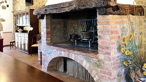 A rustic stone fireplace with a brick arch, a wooden table, and a vase with sunflowers. - Apartment 'Villa Tiberini 1' with Panoramic View, Shared Pool and Wi-Fi (Torrita di Siena)