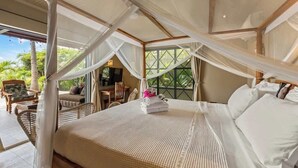 Ein Schlafzimmer mit Himmelbett, Korbmöbeln und Blick auf die grüne Umgebung.