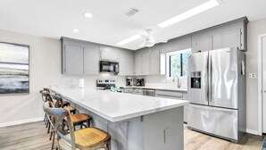 A modern kitchen with grey cabinets, a large island, stainless steel appliances, and a ceiling fan. - Walk 2 Private Beach, Private Pool, Bikes, Grayton (Santa Rosa Beach)