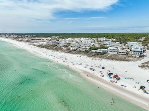An aerial view of a beach with clear turquoise waters, a sandy shore, and beachfront properties with multiple stories and balconies. - Walk 2 Private Beach, Private Pool, Bikes, Grayton (Santa Rosa Beach)