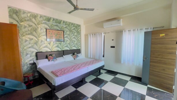 A bedroom with a bed, a ceiling fan, an air conditioning unit, a door, and a window with curtains.