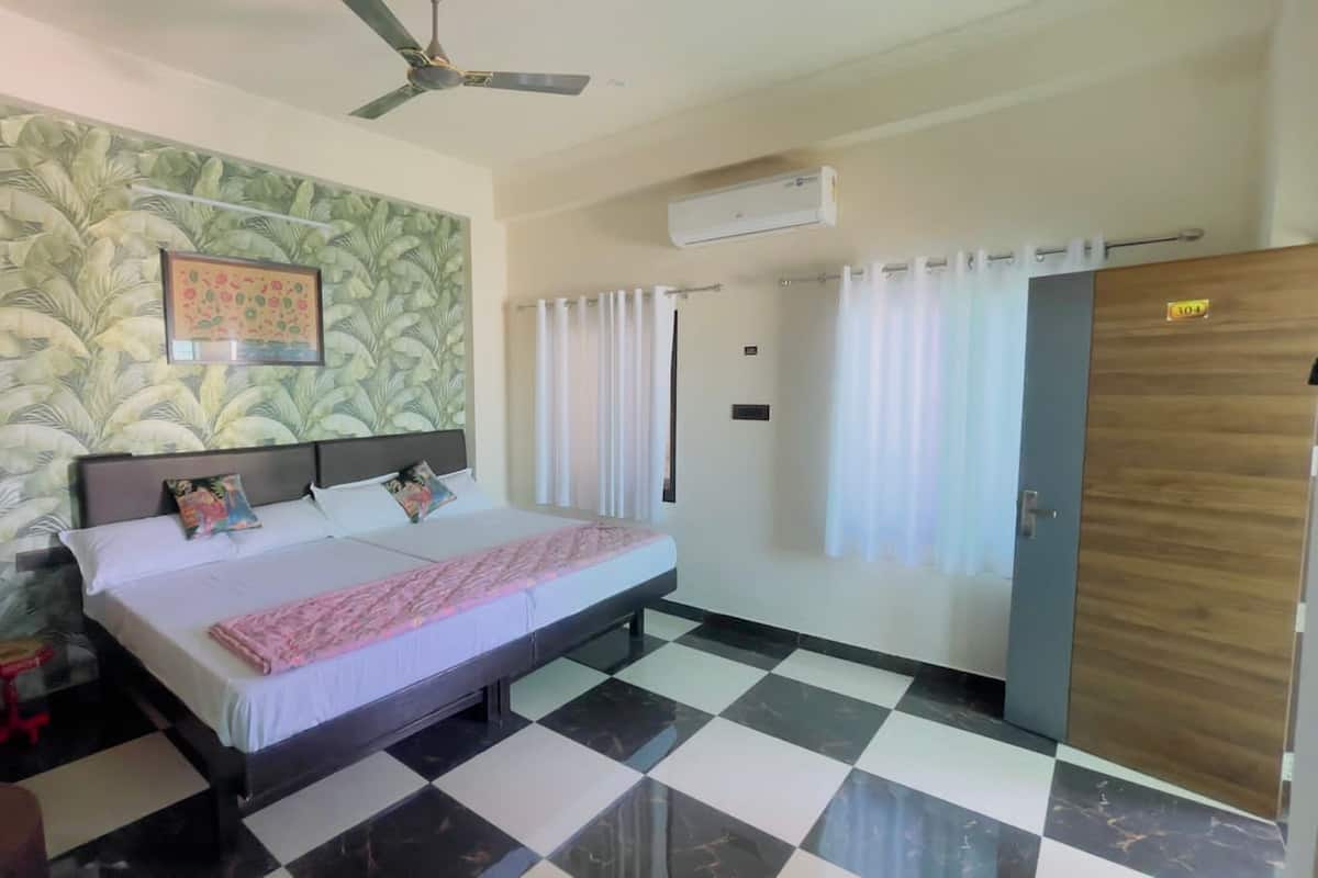 A bedroom with a bed, a ceiling fan, an air conditioning unit, a door, and a window with curtains.