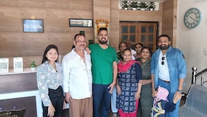 A group of people in a hotel lobby with wooden paneling, a reception desk, and a clock on the wall.