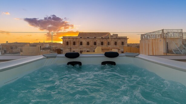 Ein Dachpool mit zwei Whirlpools, Blick auf ein historisches Gebäude und ein Sonnenuntergang im Hintergrund.