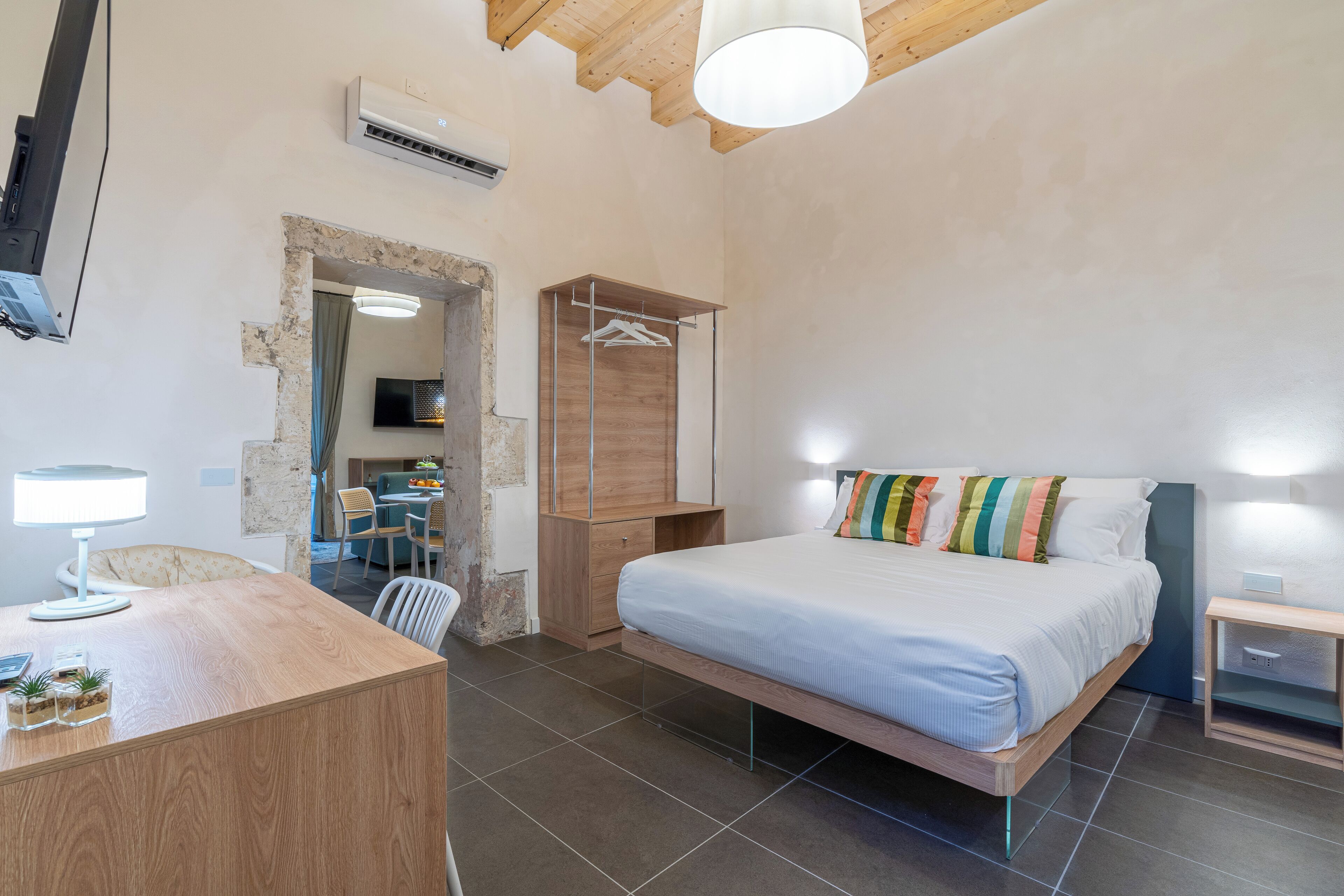 A bedroom with a bed, bedside table, and a desk with a lamp.